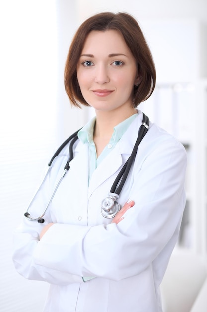 Jeune femme médecin brune debout avec les bras croisés et souriant à l'hôpital. Concept de soins de santé, d'assurance et d'aide. Médecin prêt à examiner le patient