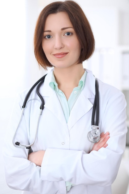 Jeune femme médecin brune debout avec les bras croisés et souriant à l'hôpital. Concept de soins de santé, d'assurance et d'aide. Médecin prêt à examiner le patient