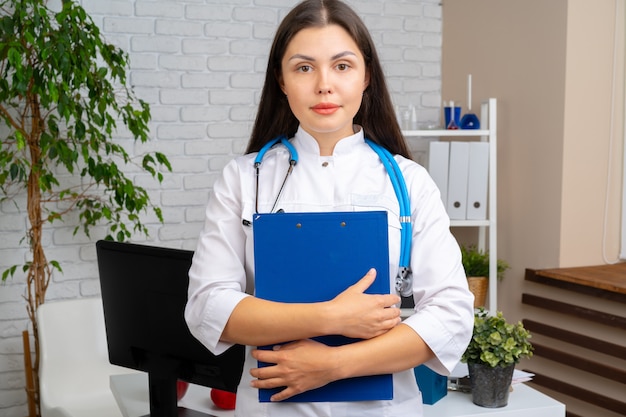 Jeune femme médecin brune debout avec le presse-papier dans son bureau