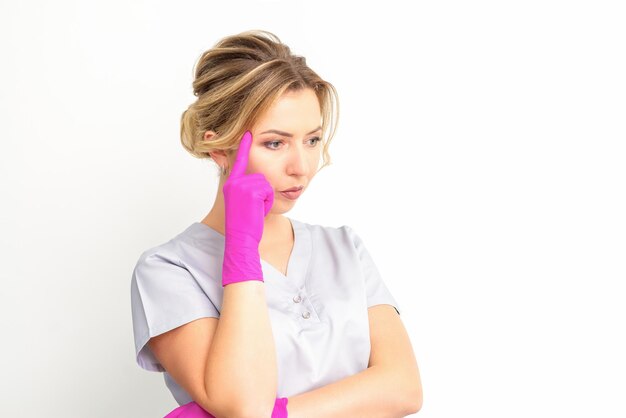 Jeune femme médecin caucasien portant des gants pensif regardant loin isolé sur fond blanc