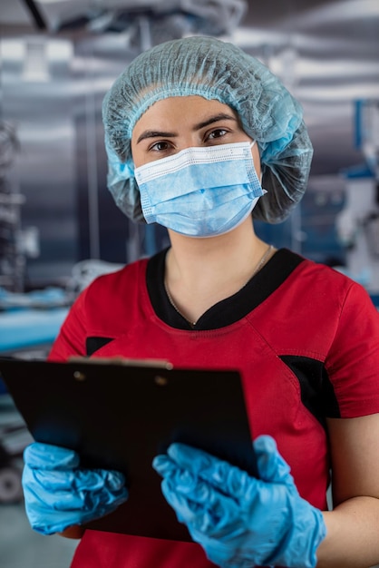 Photo jeune femme médecin caucasienne portant un uniforme médical rouge avec stéthoscope et masque tenant un bloc-notes concept médical