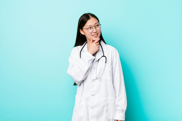 Jeune femme médecin chinoise regardant de côté avec une expression douteuse et sceptique.