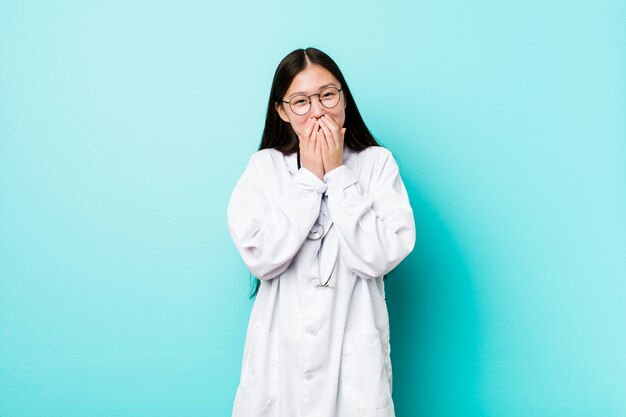 Jeune femme médecin chinoise rire de quelque chose, couvrant la bouche avec les mains.