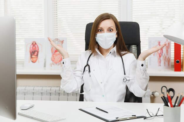 Jeune Femme Médecin Choquée Assise Au Bureau écartant Les Mains Travaillant Avec Des Documents Médicaux Dans Un Bureau Léger à L'hôpital