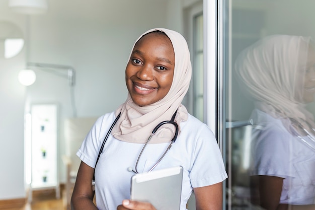 Jeune femme médecin clinicienne africaine musulmane en gommage utilisant le pavé tactile tout en communiquant avec les patients en ligne