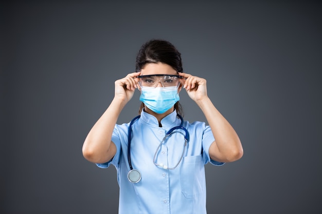 Jeune femme médecin dédiée avec masque protecteur mettant des lunettes de protection.