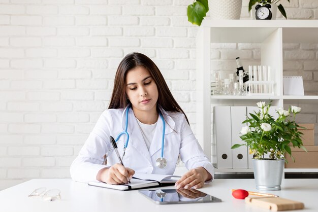 Jeune femme médecin écrivant dans son cabinet remplissant les antécédents médicaux ou l'anamnèse