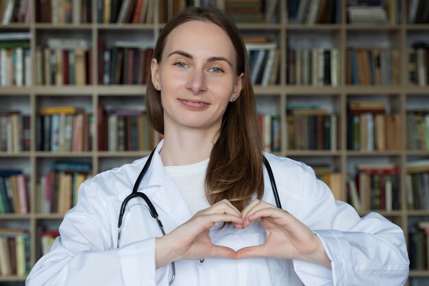 Jeune femme médecin faisant signe de coeur avec ses mains contre une étagère