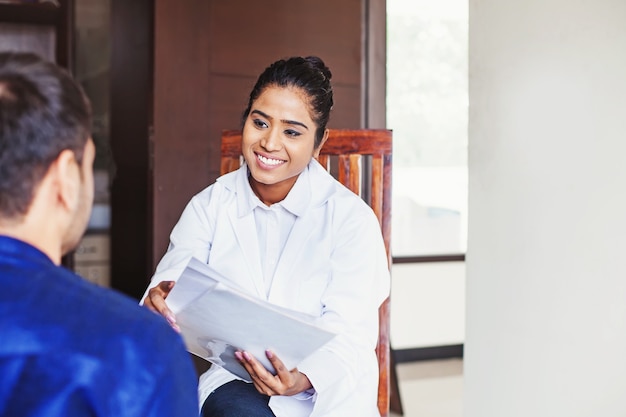 Jeune femme médecin indienne consultant un patient tout en tenant des rapports médicaux dans ses mains