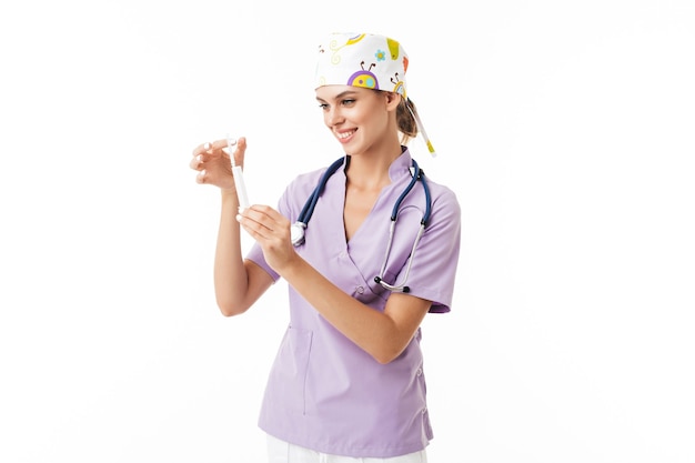 Jeune femme médecin joyeuse en uniforme avec phonendoscope sur le cou tenant la seringue dans les mains tout en heureusement