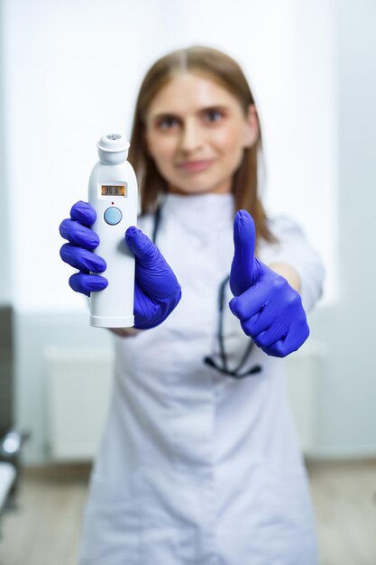 Une jeune femme médecin mesure sa température avec un thermomètre électronique sans contact