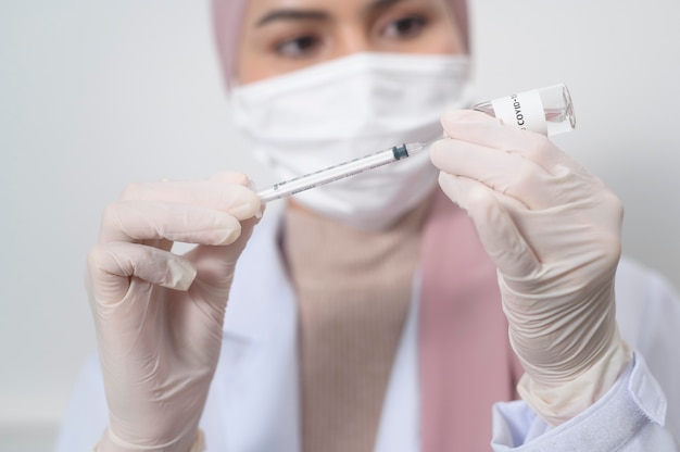 Une jeune femme médecin musulmane tenant une seringue avec une bouteille de vaccin covid-19 pour injection, vaccination covid-19 et concept de soins de santé