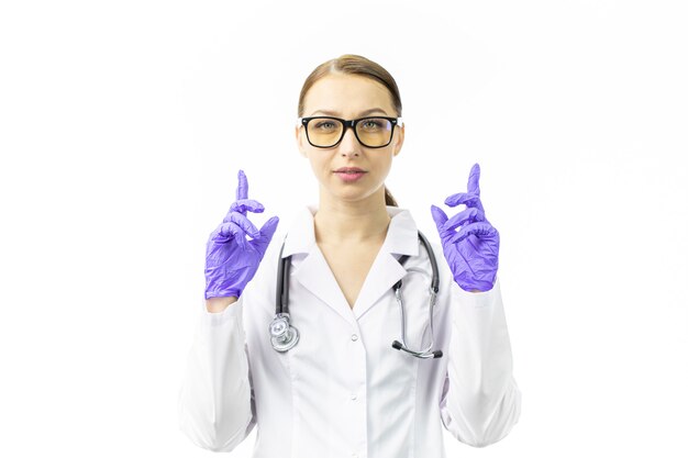Jeune femme médecin pointant ses index vers le haut dans des gants bleus