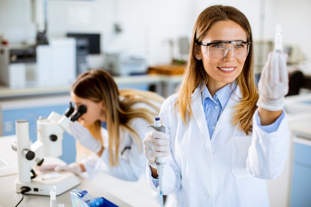 Jeune Femme Médecin Portant Un Masque Protecteur En Laboratoire Tenant Un Flacon Avec Un échantillon Liquide