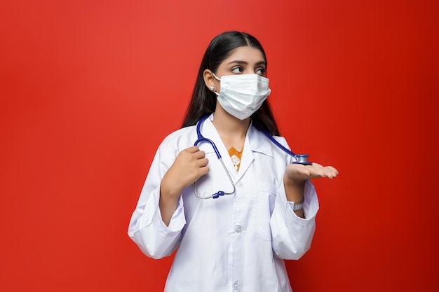 jeune femme médecin portant un masque, tenant un stéthoscope sur fond rouge modèle pakistanais indien