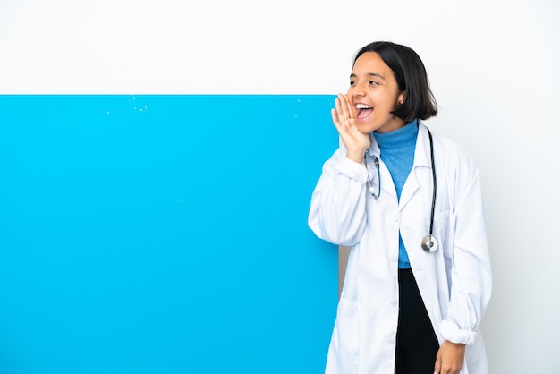 Jeune femme médecin de race mixte avec une grande pancarte isolée sur fond blanc en criant avec la bouche grande ouverte sur le côté