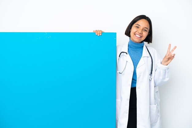 Jeune femme médecin de race mixte avec une grande pancarte isolée sur fond blanc souriant et montrant le signe de la victoire