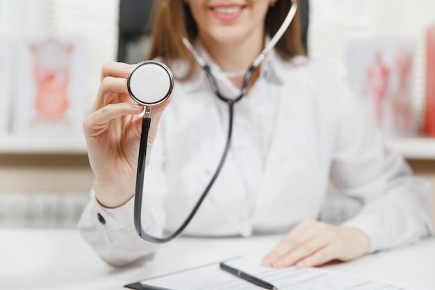 Jeune femme médecin souriante assise au bureau, travaillant avec des documents médicaux dans un bureau léger à l'hôpital