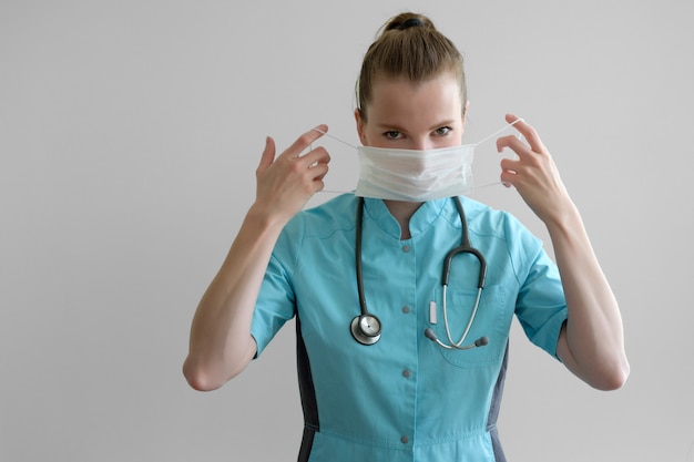 Jeune femme médecin avec stéthoscope attires masque de protection isolé sur gris