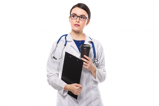 Jeune femme médecin avec stéthoscope tenant le presse-papiers et une tasse de café dans ses mains