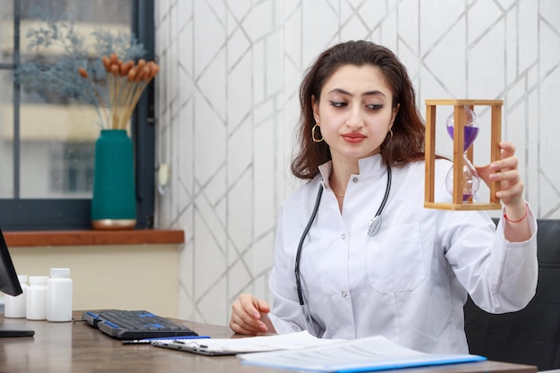 Jeune femme médecin tenant une horloge de sable et regardant tiot Photo de haute qualité