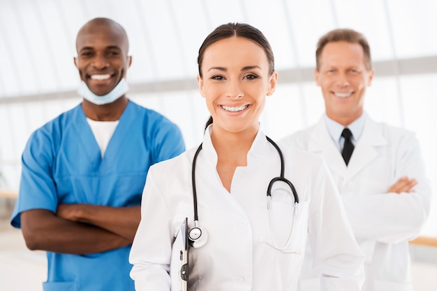 Photo jeune femme médecin à la tête de son équipe. belle femme médecin tenant un presse-papiers et souriant tandis que ses collègues se tiennent derrière elle en arrière-plan