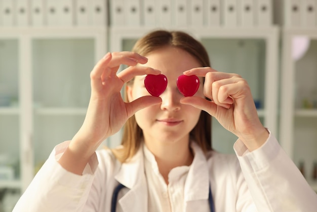 Jeune femme médecin tient des coeurs rouges avec les mains contre les yeux femme positive en professionnel