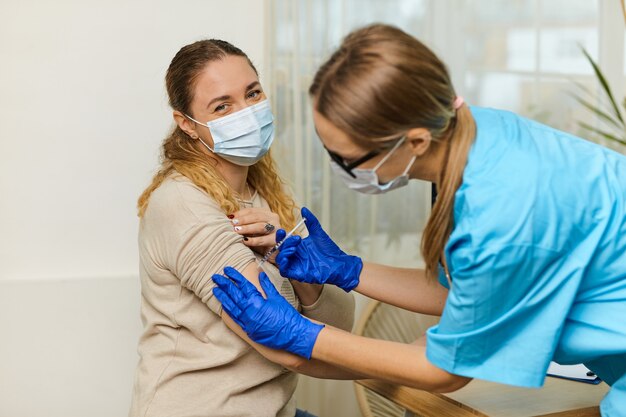 Une jeune femme médecin vaccine contre le coronavirus Covid 19 à une jeune femme dans le bureau d'une clinique médicale