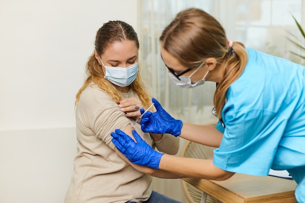 Une jeune femme médecin vaccine contre le coronavirus Covid 19 à une jeune femme dans le bureau d'une clinique médicale