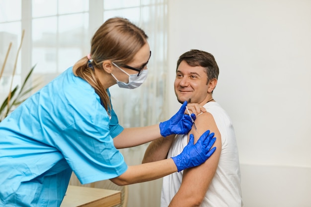 Une jeune femme médecin vaccine contre le coronavirus Covid 19 à un jeune homme dans le bureau d'une clinique médicale