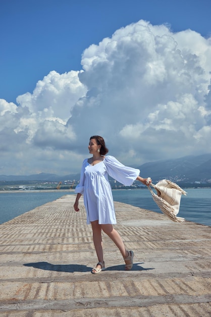 Une jeune femme méditerranéenne ensoleillée exhale beauté et grâce sur un fond de mer azur et de montagnes côtières. Les cheveux brunes encadrent un portrait attrayant des loisirs au bord de la mer.