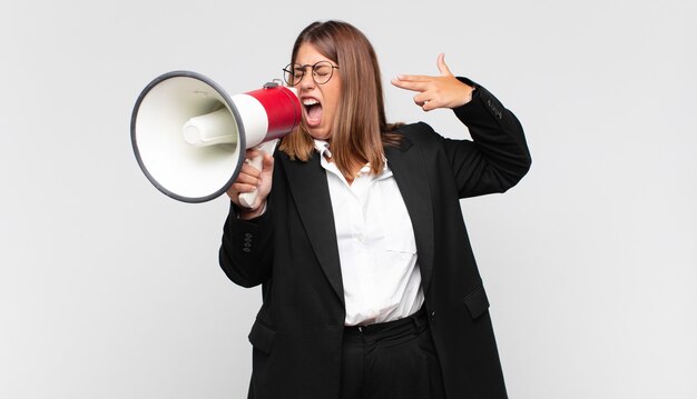 Jeune femme avec un mégaphone à la malheureuse et stressée, geste de suicide faisant signe des armes à feu avec la main, pointant vers la tête