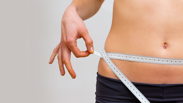 Jeune femme mesurant son tour de taille dans une salle de sport avec un ruban
