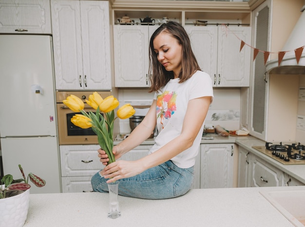 Une jeune femme met joyeusement des tulipes jaunes colorées fraîches dans un vase transparent