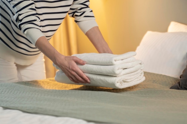 Une jeune femme met une pile de serviettes de bain blanches fraîches sur un drap. Le service de chambre nettoie l'hôtel.