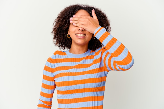 Jeune femme métisse afro-américaine isolée couvre les yeux avec les mains, sourit largement en attente d'une surprise.