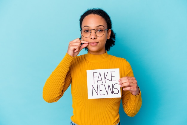 Jeune femme métisse afro-américaine tenant un concept de fake news avec les doigts sur les lèvres en gardant un secret.