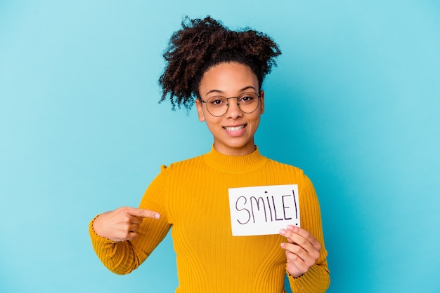 Jeune femme métisse afro-américaine tenant un concept de sourire personne pointant à la main vers un espace de copie de chemise, fier et confiant