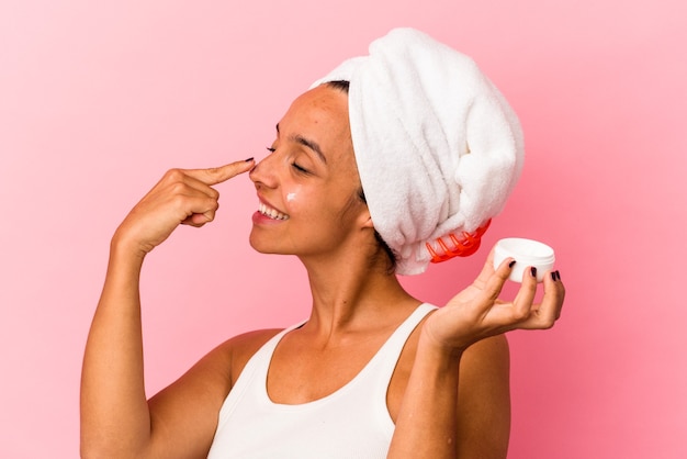 Jeune femme métisse appliquant de la crème sur son visage isolé