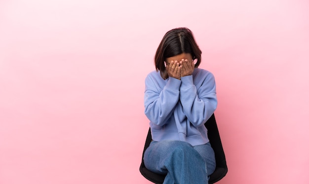 Jeune femme métisse assise sur une chaise isolée sur fond rose avec une expression fatiguée et malade