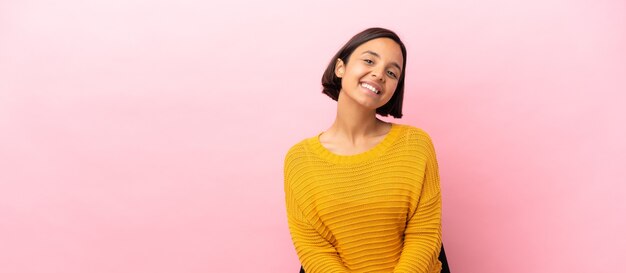 Jeune femme métisse assise sur une chaise isolée sur fond rose en riant