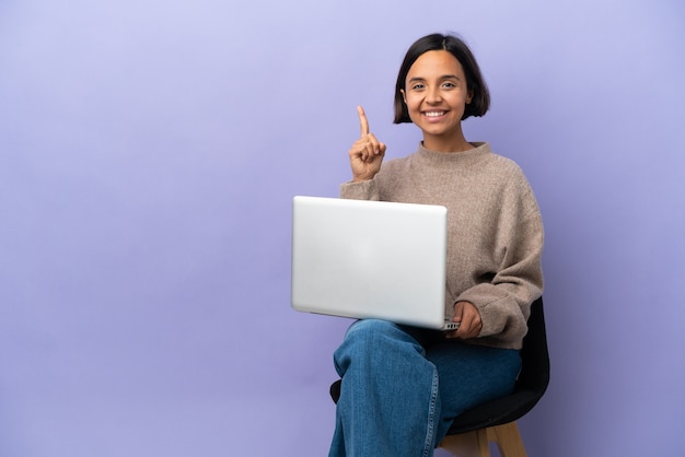 Jeune femme métisse assise sur une chaise avec un ordinateur portable isolé pointant vers une excellente idée