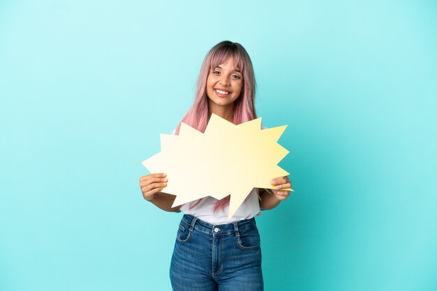 Jeune femme métisse aux cheveux roses isolée sur fond bleu tenant une bulle de dialogue vide