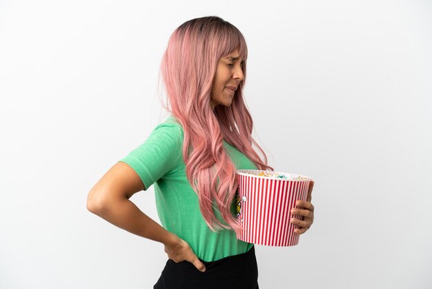 Jeune femme métisse aux cheveux roses mangeant du pop-corn isolé sur fond blanc souffrant de maux de dos pour avoir fait un effort