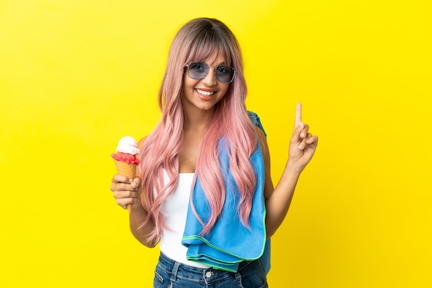 Jeune Femme Métisse Aux Cheveux Roses Tenant Une Glace Isolée Sur Fond Jaune Pointant Vers Une Excellente Idée