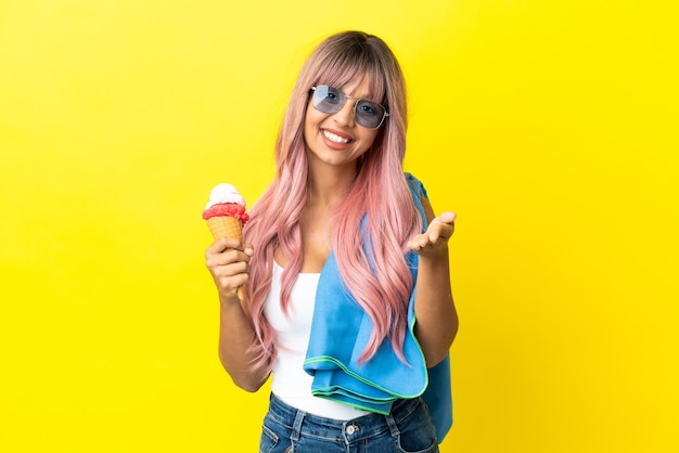 Jeune femme métisse aux cheveux roses tenant une glace isolée sur fond jaune se serrant la main pour conclure une bonne affaire