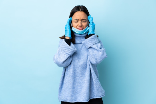 Jeune femme métisse brune protégeant avec un masque et des gants sur le mur bleu avec des maux de tête