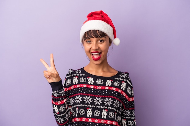 Jeune femme métisse célébrant Noël isolé sur fond violet joyeux et insouciant montrant un symbole de paix avec les doigts.