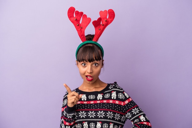 Jeune femme métisse avec chapeau de renne célébrant Noël isolé sur fond violet ayant une idée, concept d'inspiration.