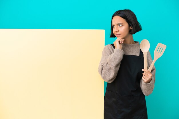 Jeune femme métisse de cuisinier avec une grande pancarte isolée sur fond bleu et levant